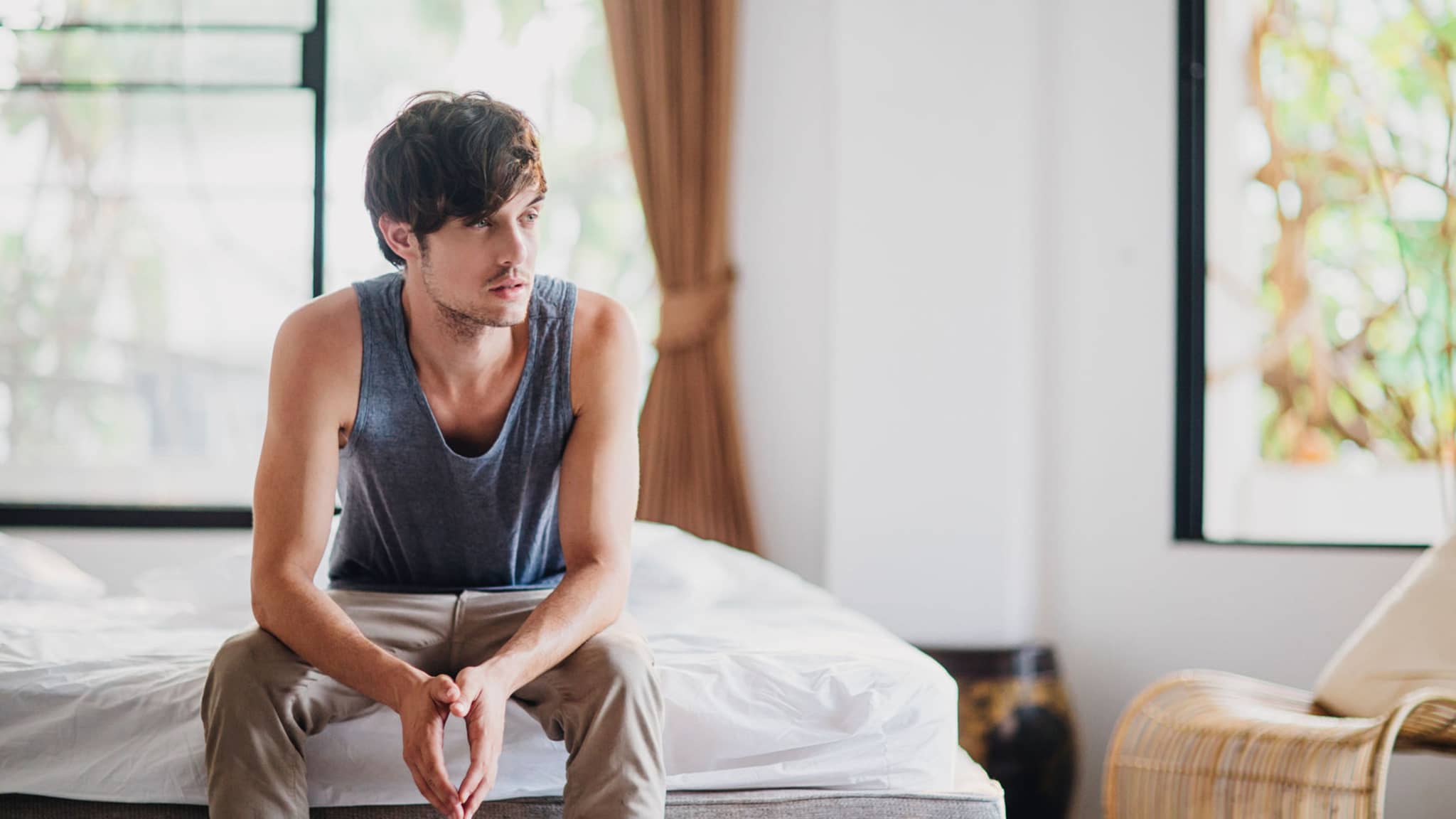 Erkrankungen: Junger Mann sitzt krank auf seinem Bett.