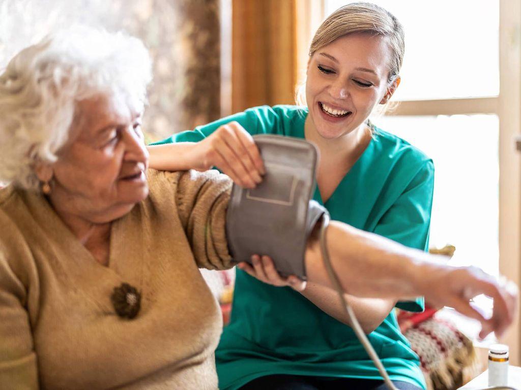 Pflegeversicherung: Pflegerin legt einer älteren Frau eine Blutdruckmanschette an