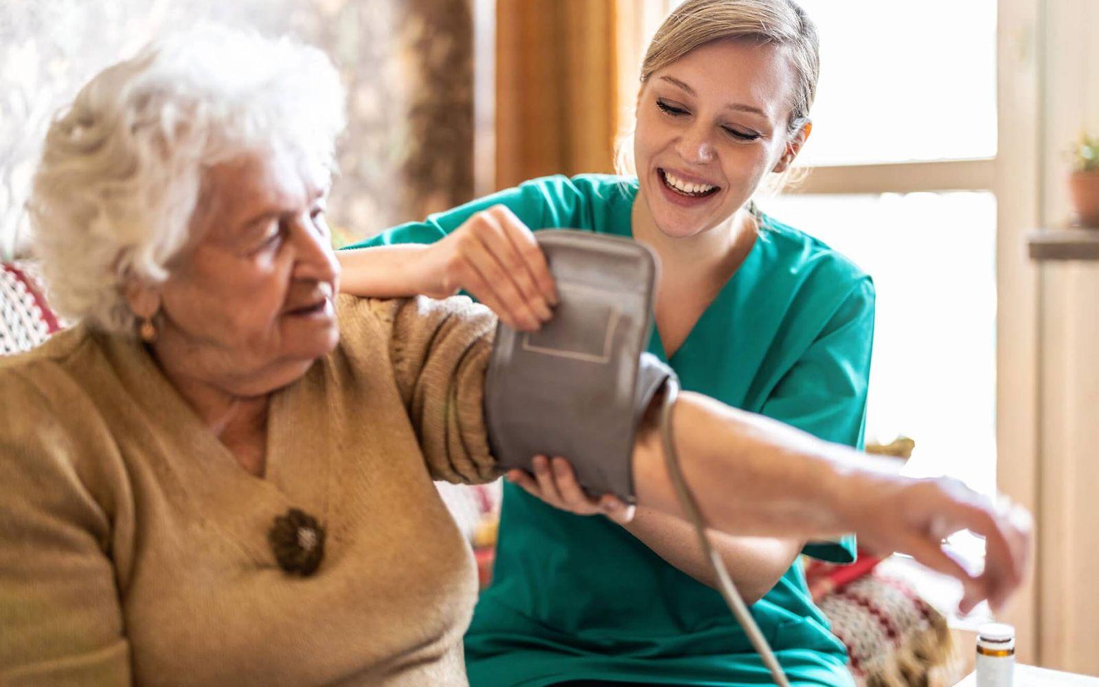 Pflegeversicherung: Pflegerin legt einer älteren Frau eine Blutdruckmanschette an