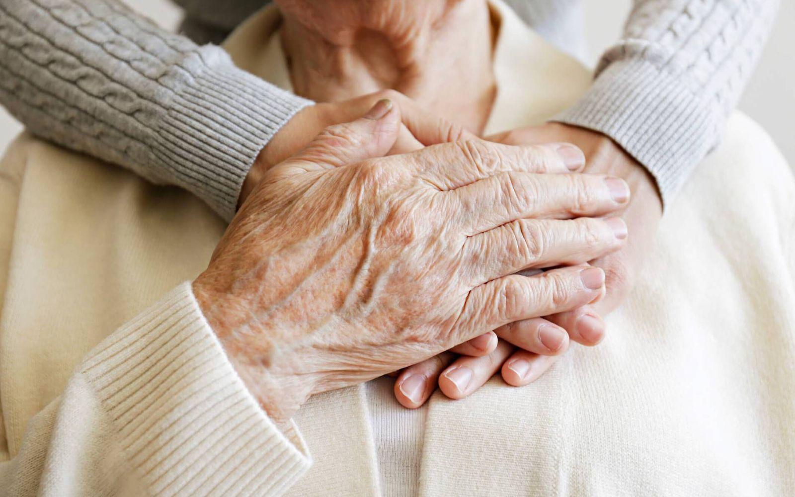 Körperpflege, Ernährung, Bewegung bei häuslicher Pflege: Hand einer älteren Frau hält eine jüngere an ihre Brust