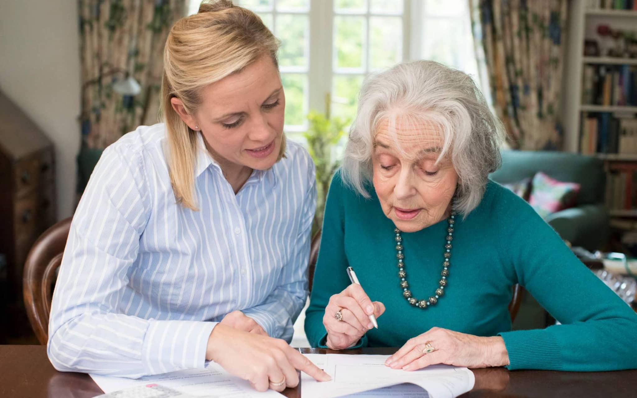 Formales im Pflegealltag: Eine Frau hilft einer älteren Dame beim Papierkram