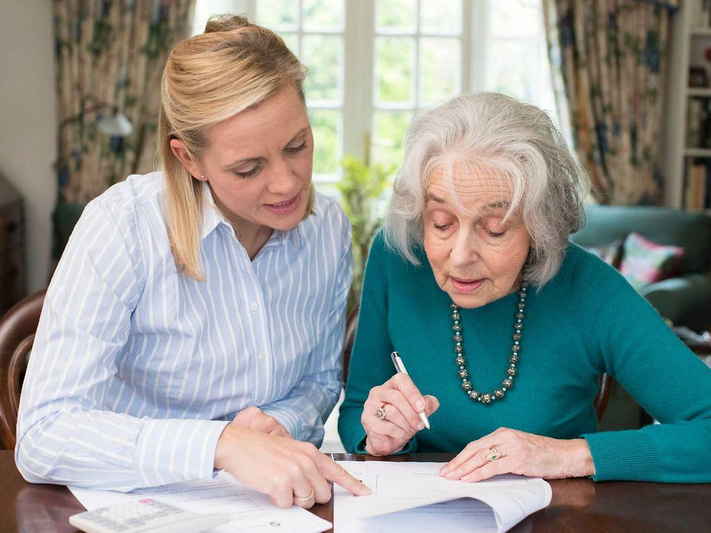 Formales im Pflegealltag: Eine Frau hilft einer älteren Dame beim Papierkram