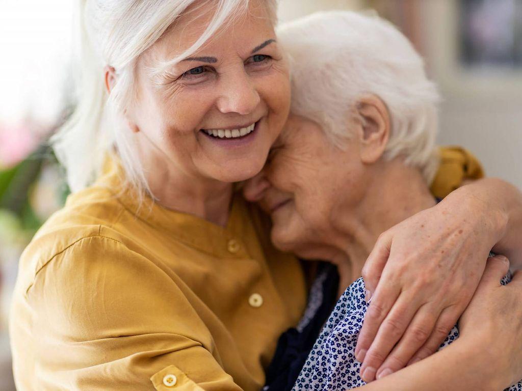 Absicherung für pflegende Angehörige: Frau und Mutter liegen sich lächelnd in den Armen