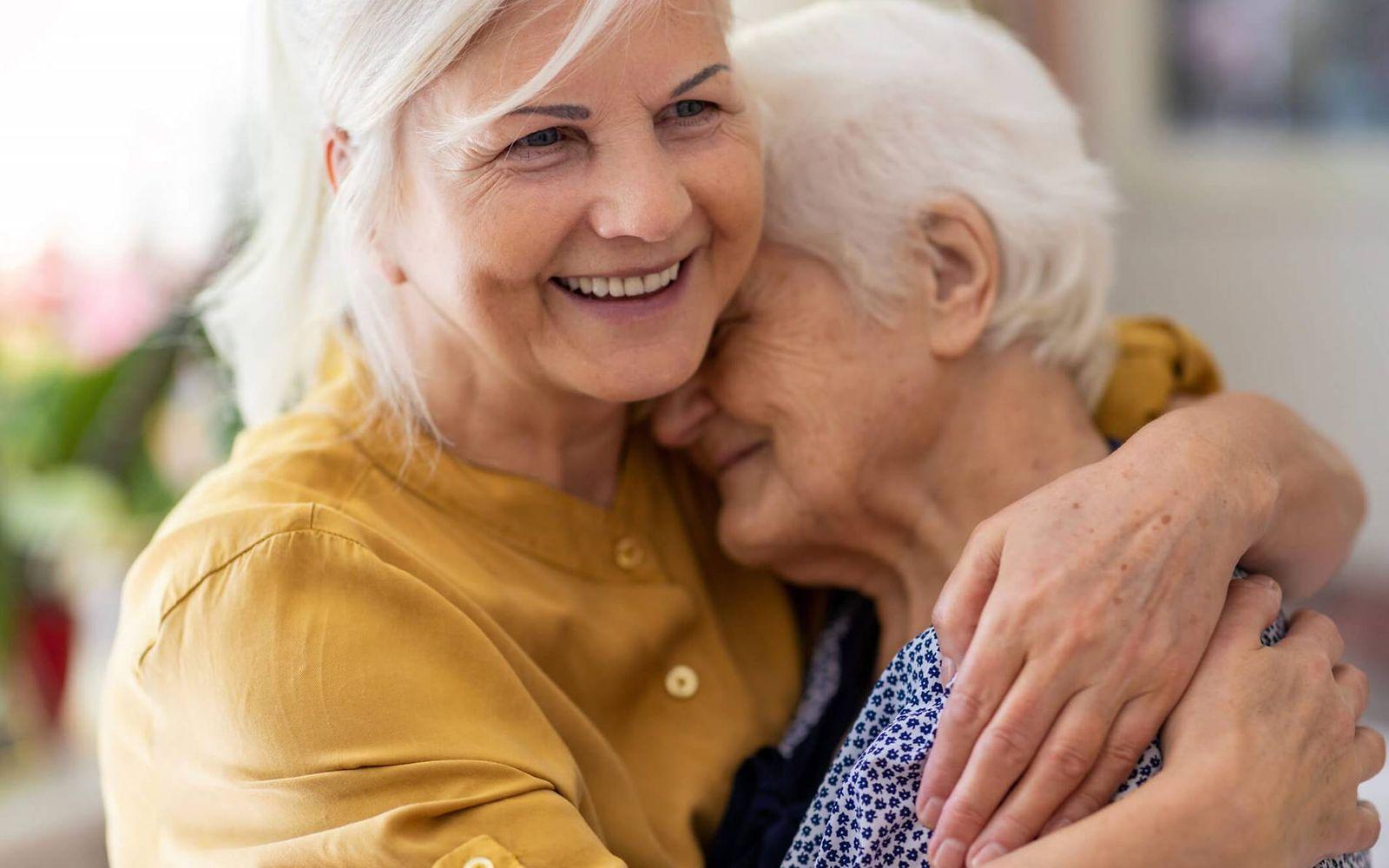 Absicherung für pflegende Angehörige: Frau und Mutter liegen sich lächelnd in den Armen