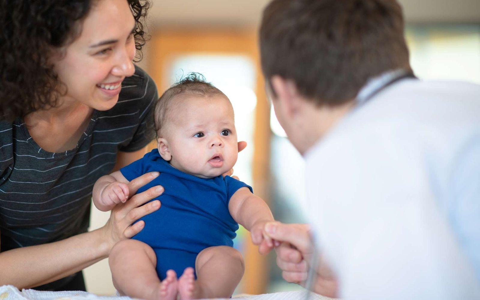 Bonusprogramm für Babys: Eine Mutter hält Ihr Baby bei einer Vorsorgeuntersuchung beim Arzt fest.