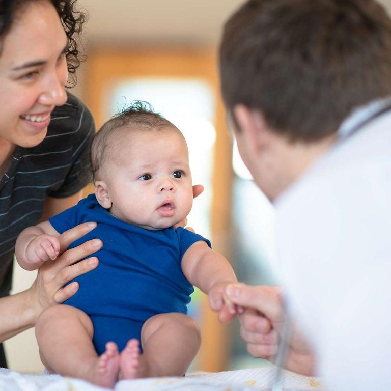 Bonusprogramm für Babys: Eine Mutter hält Ihr Baby bei einer Vorsorgeuntersuchung beim Arzt fest.