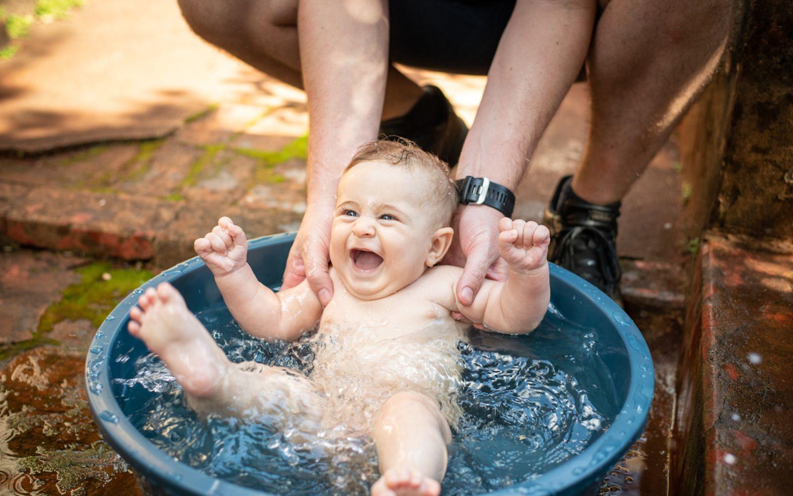 Babys und Hitze: Vater badet sein Baby draußen in einer kleinen Wanne