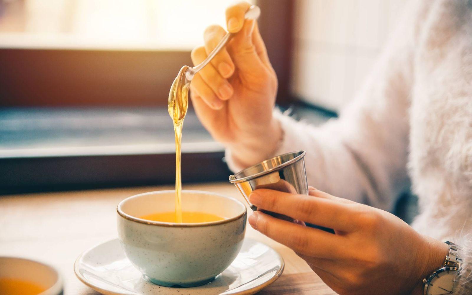 Zuckerersatz: Frau süßt ihren Tee mit einem Löffel Honig