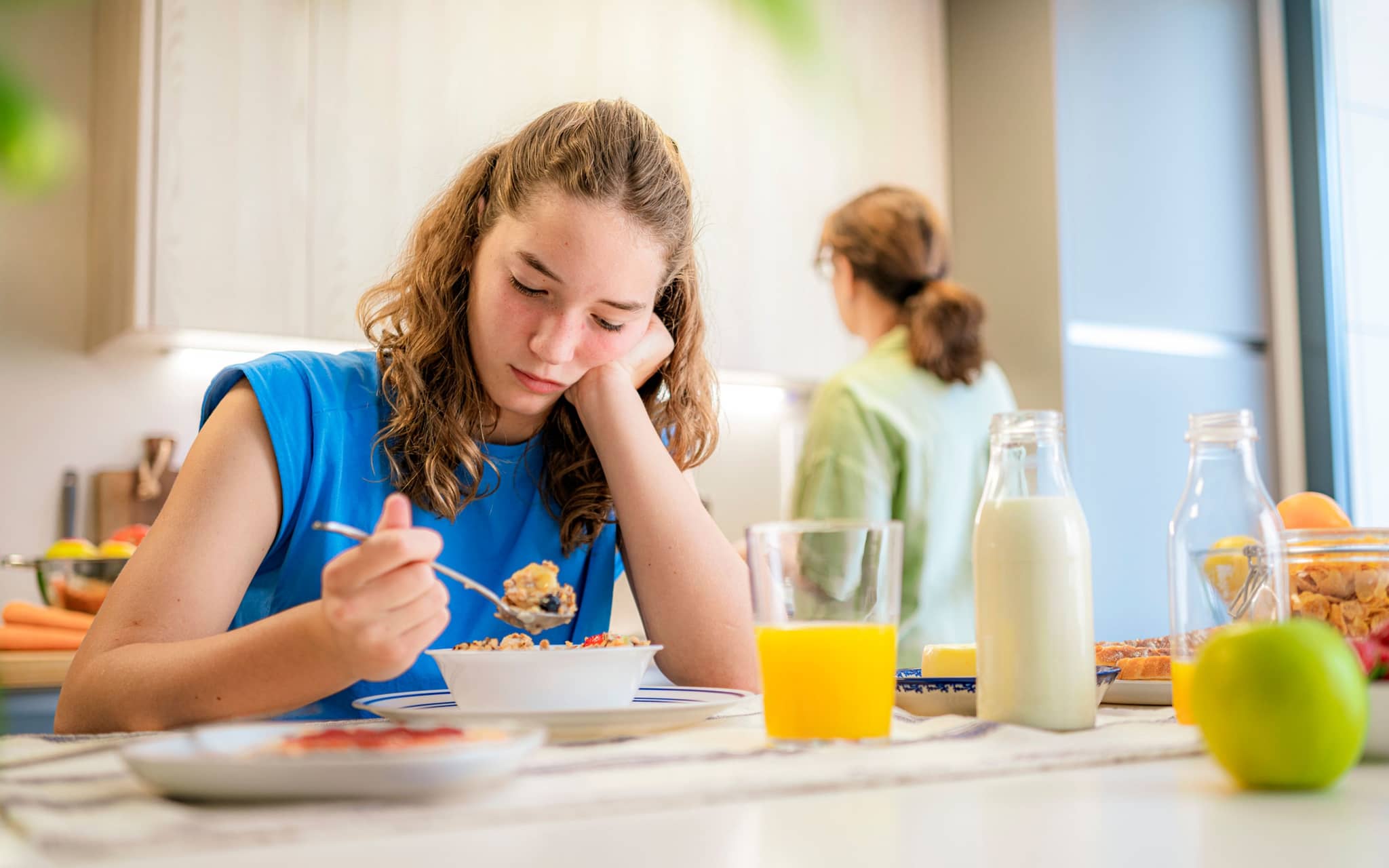 Esstörungen bei Kindern: Ein Mädchen im Teenageralter sitzt lustlos vor ihrer Müslischale