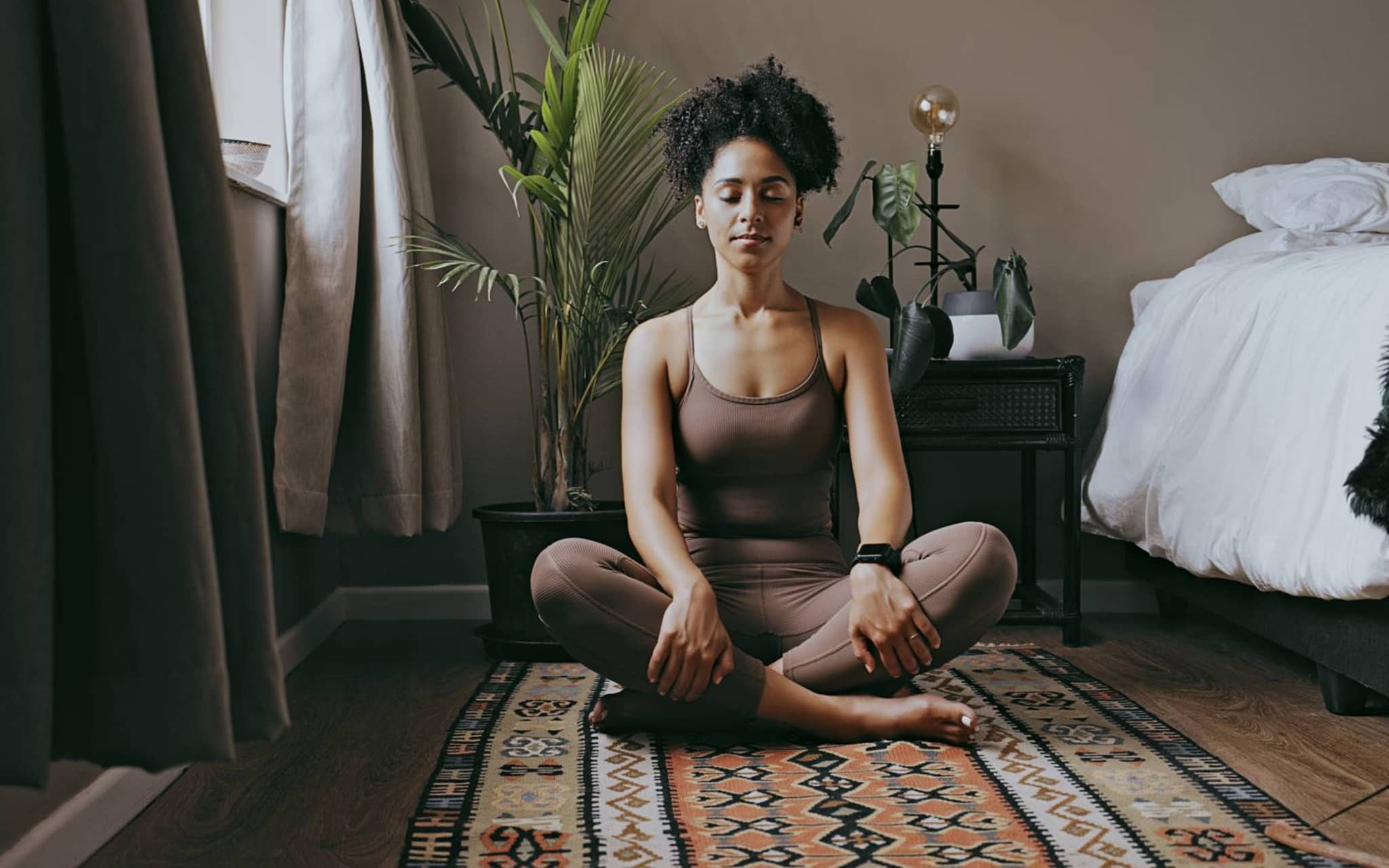 Meditation: Junge Frau sitzt im Schneidersitz auf dem Boden und hält die Augen geschlossen