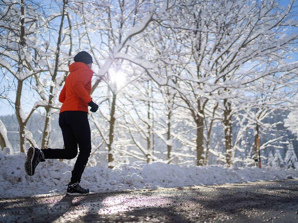 Laufen bei Kälte: Frau läuft eine verschneite Straße entlang
