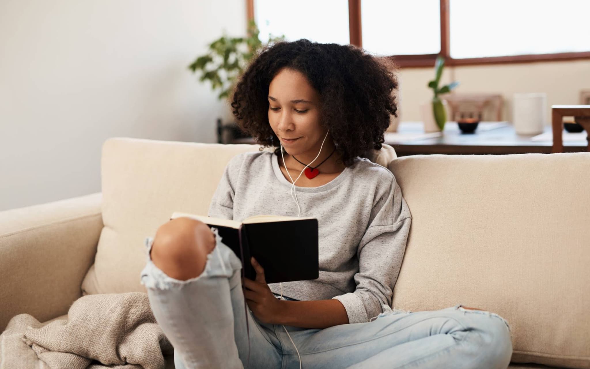 Tagebuch schreiben: Junge Frau sitzt entspannt auf der Couch und schreibt in ein Buch