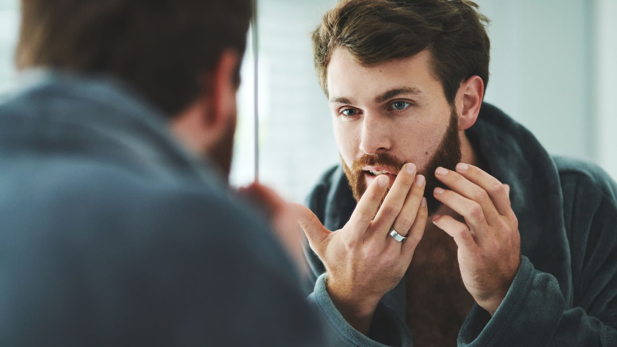 Symbolbild: Mann prüft seine Haut kritisch im Spiegel.