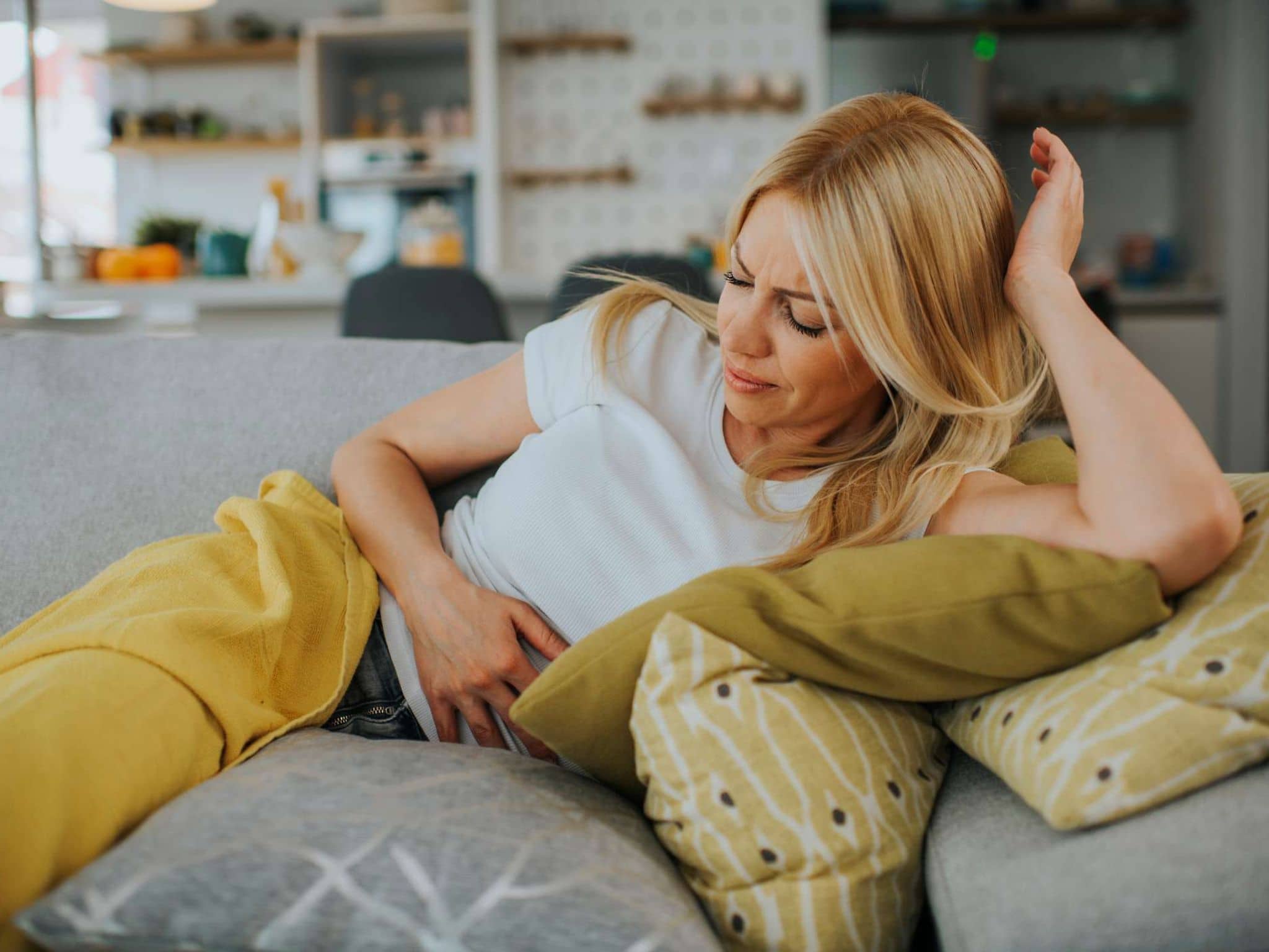 Symbolbild Völlegefühl nach dem Essen: Frau liegt auf dem Sofa und fasst sich an den Bauch.