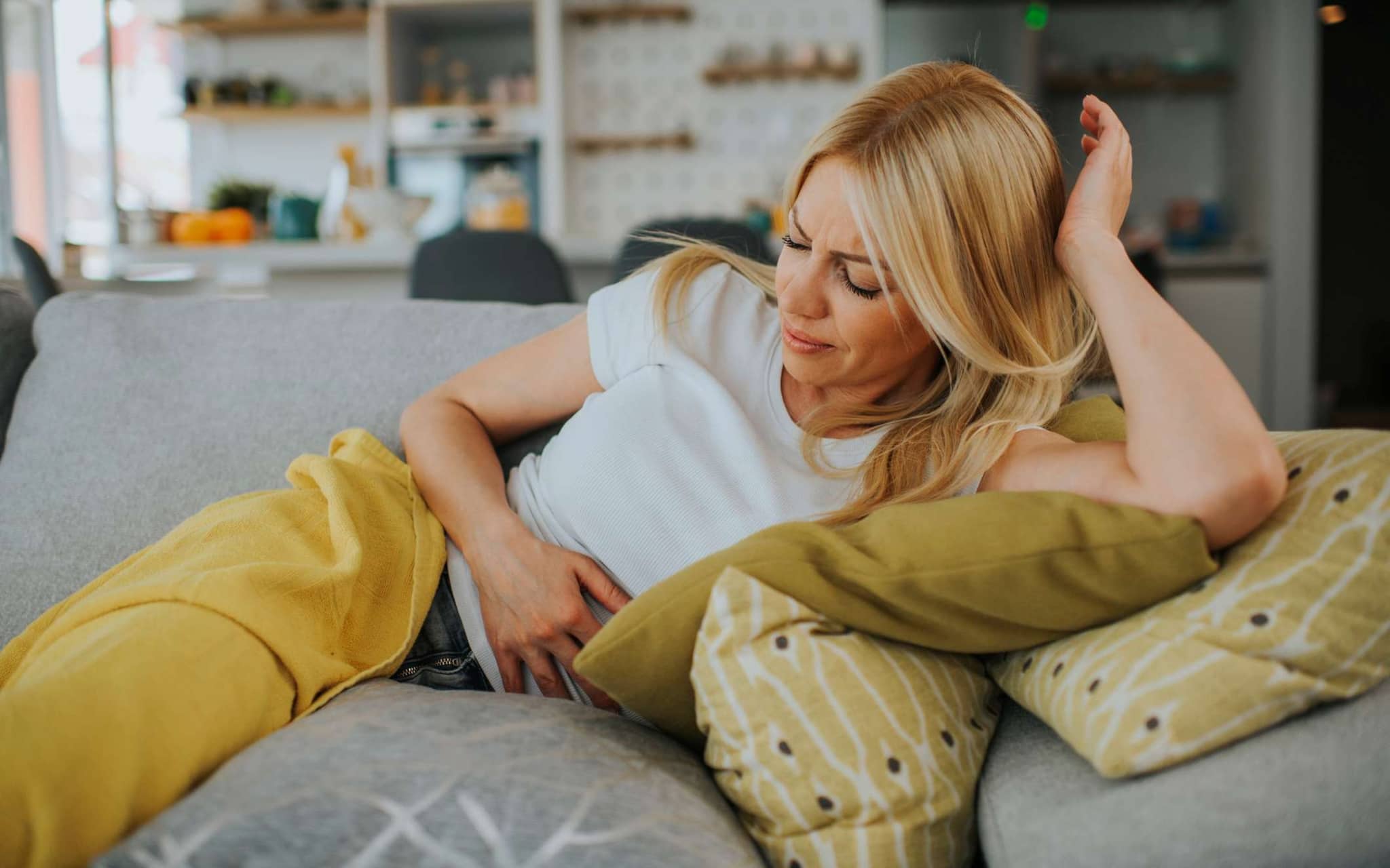 Symbolbild Völlegefühl nach dem Essen: Frau liegt auf dem Sofa und fasst sich an den Bauch.