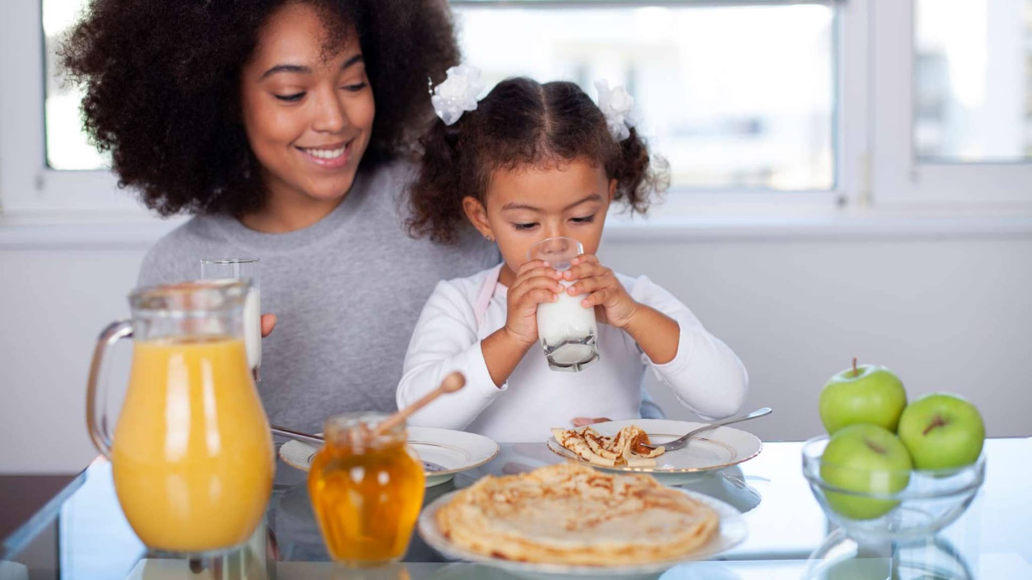 Trinken: Mutter und Tochter frühstücken in der Küche und trinken dabei Milch.
