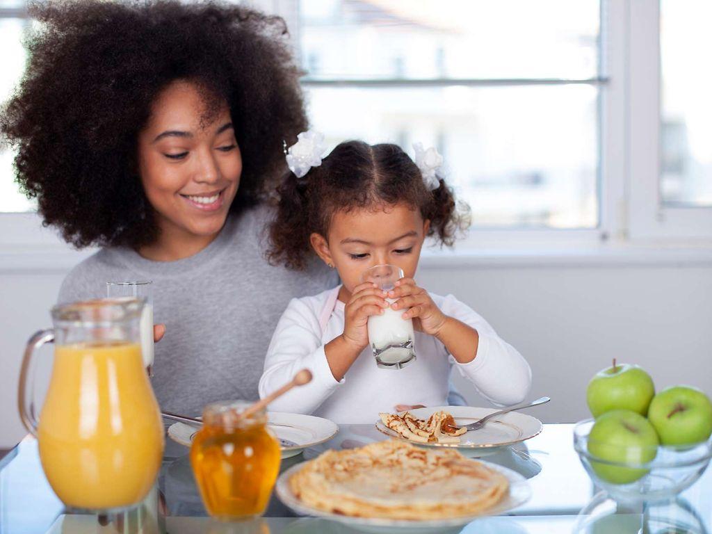 Trinken: Mutter und Tochter frühstücken in der Küche und trinken dabei Milch.