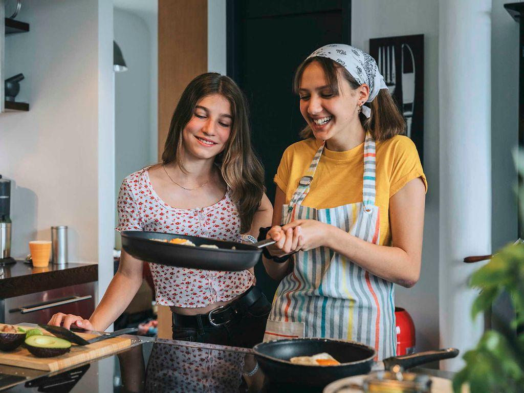 Bild: Zwei jugendliche Mädchen braten in der Küche Eier.