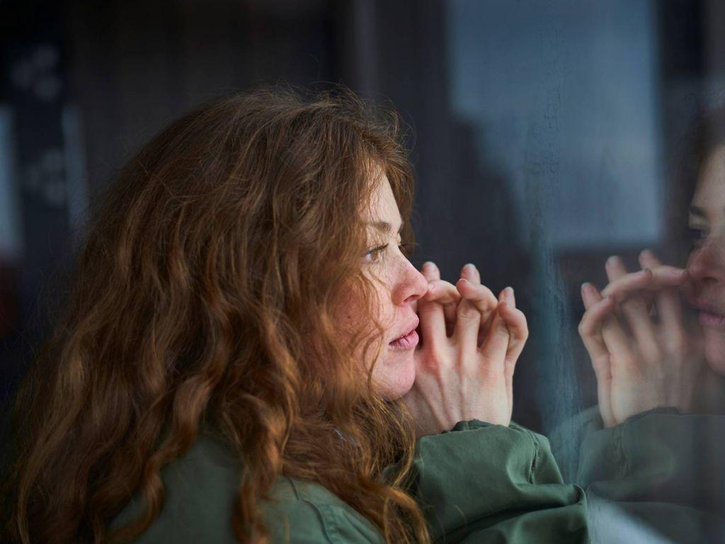 Symbolbild psychische Erkrankungen: Junge Frau schaut sorgenvoll aus dem Fenster