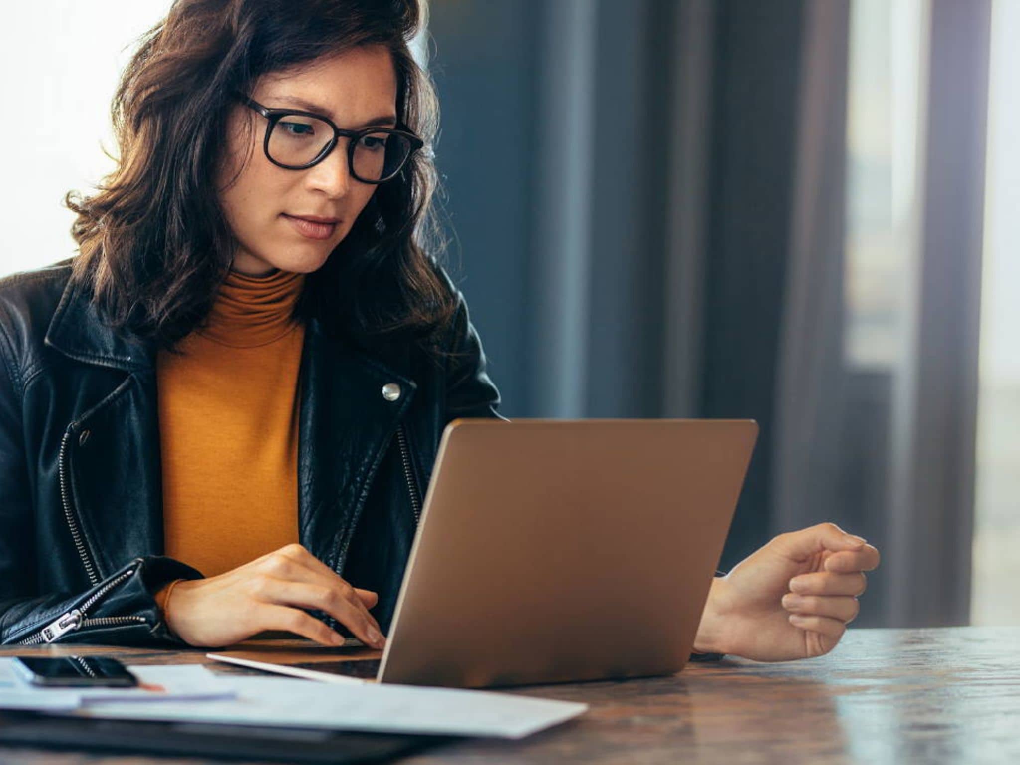 Bild: Frau mit Lederjacke und Brille schaut etwas auf Ihrem Laptop nach.