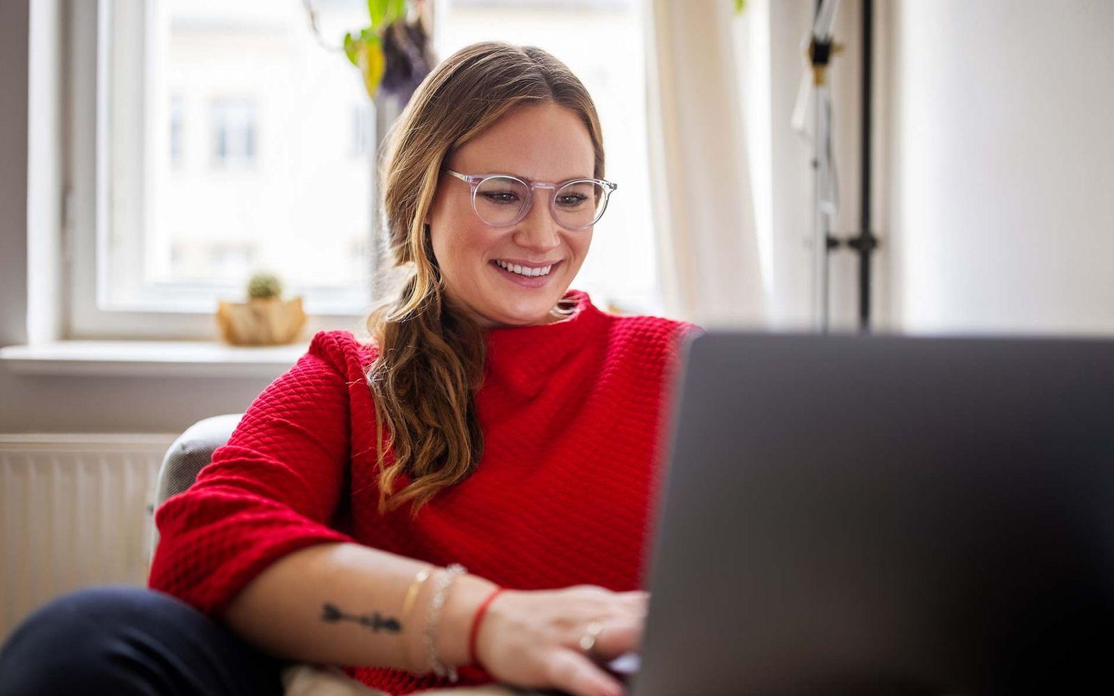 Bild: Junge Frau mit rotem Pullover schaut in Ihren Laptop.