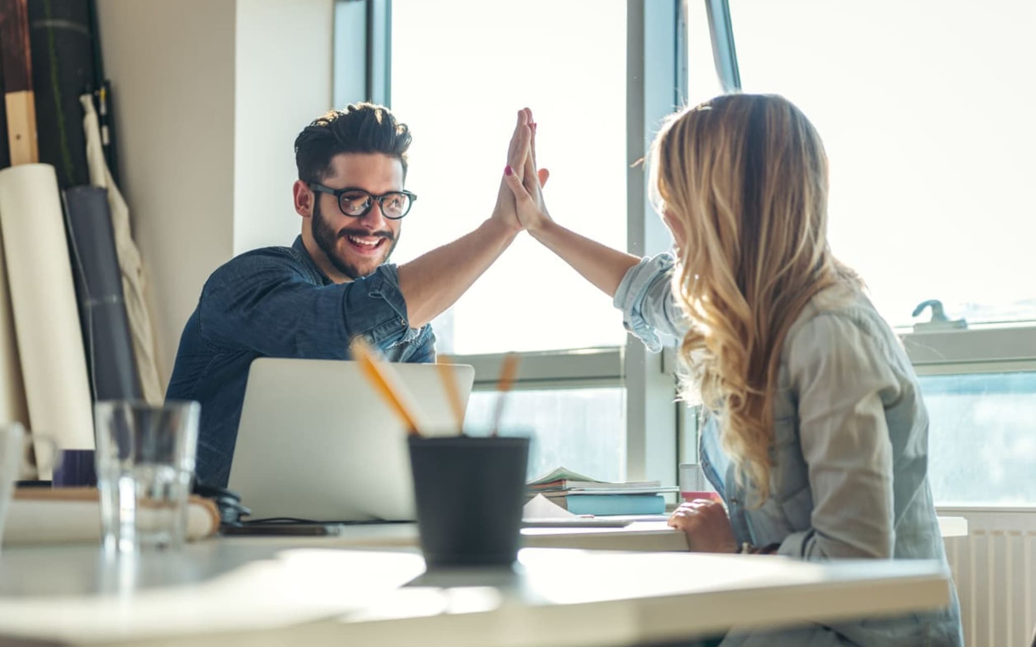 Bild: Frau und Mann geben sich ein High-Five am Schreibtisch.