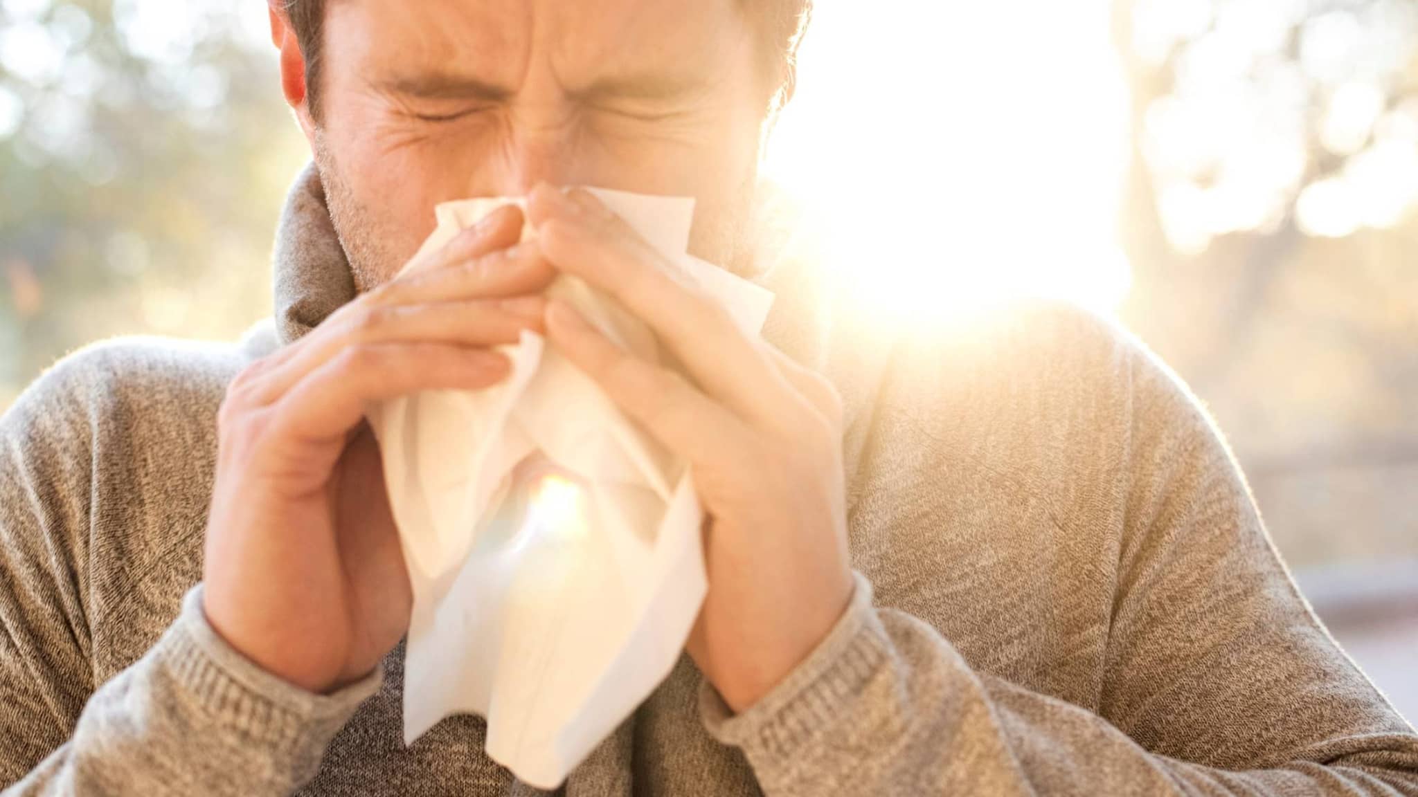 Ein Mann niest in ein Taschentuch aufgrund seiner Allergie.