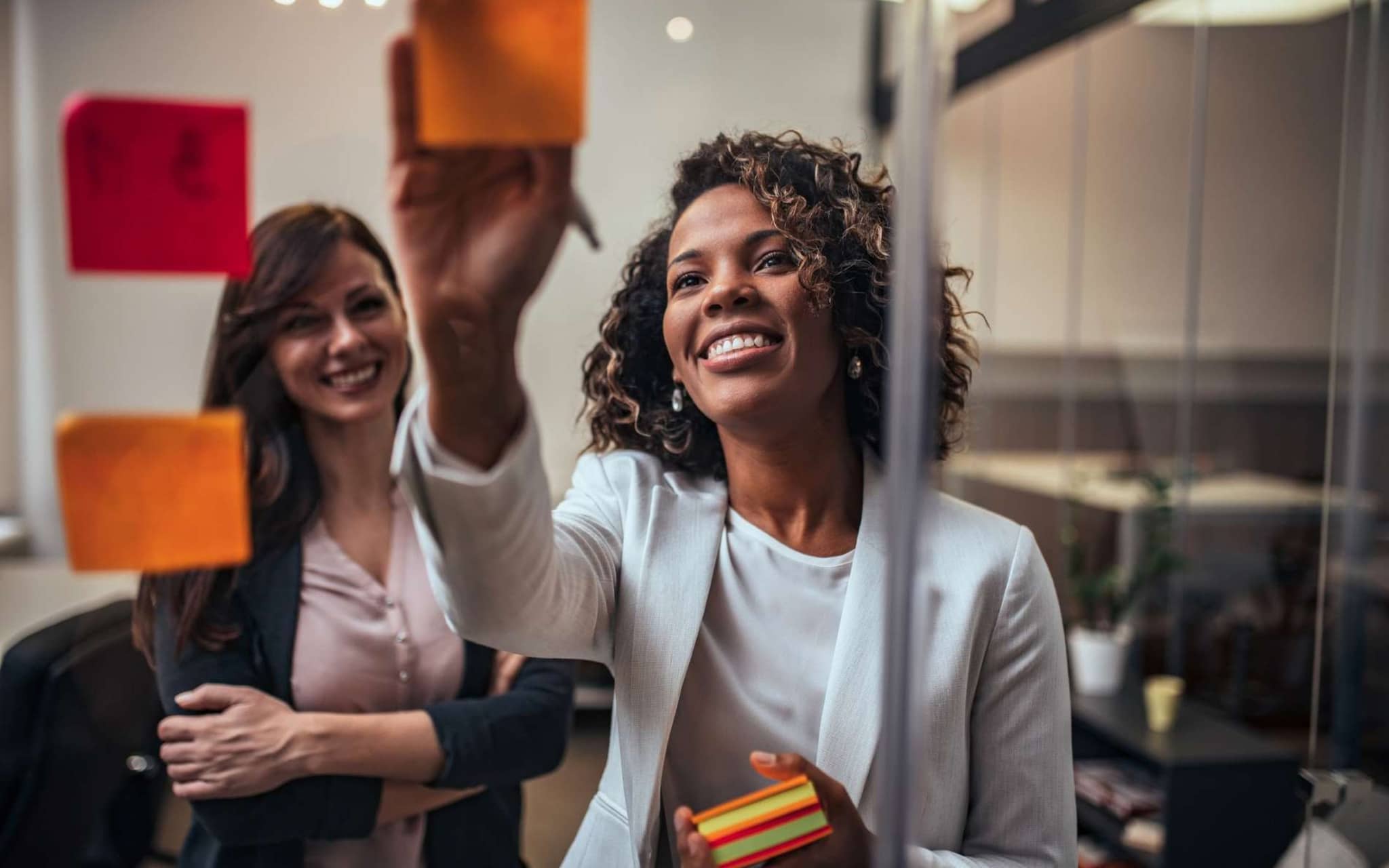 Bild: Frau klebt Post ist an eine Glaswand und lächelt.