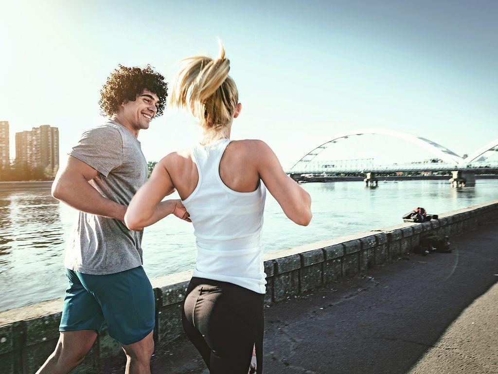 Bild: Mann und Frau joggen an einem Flussufer entlang.