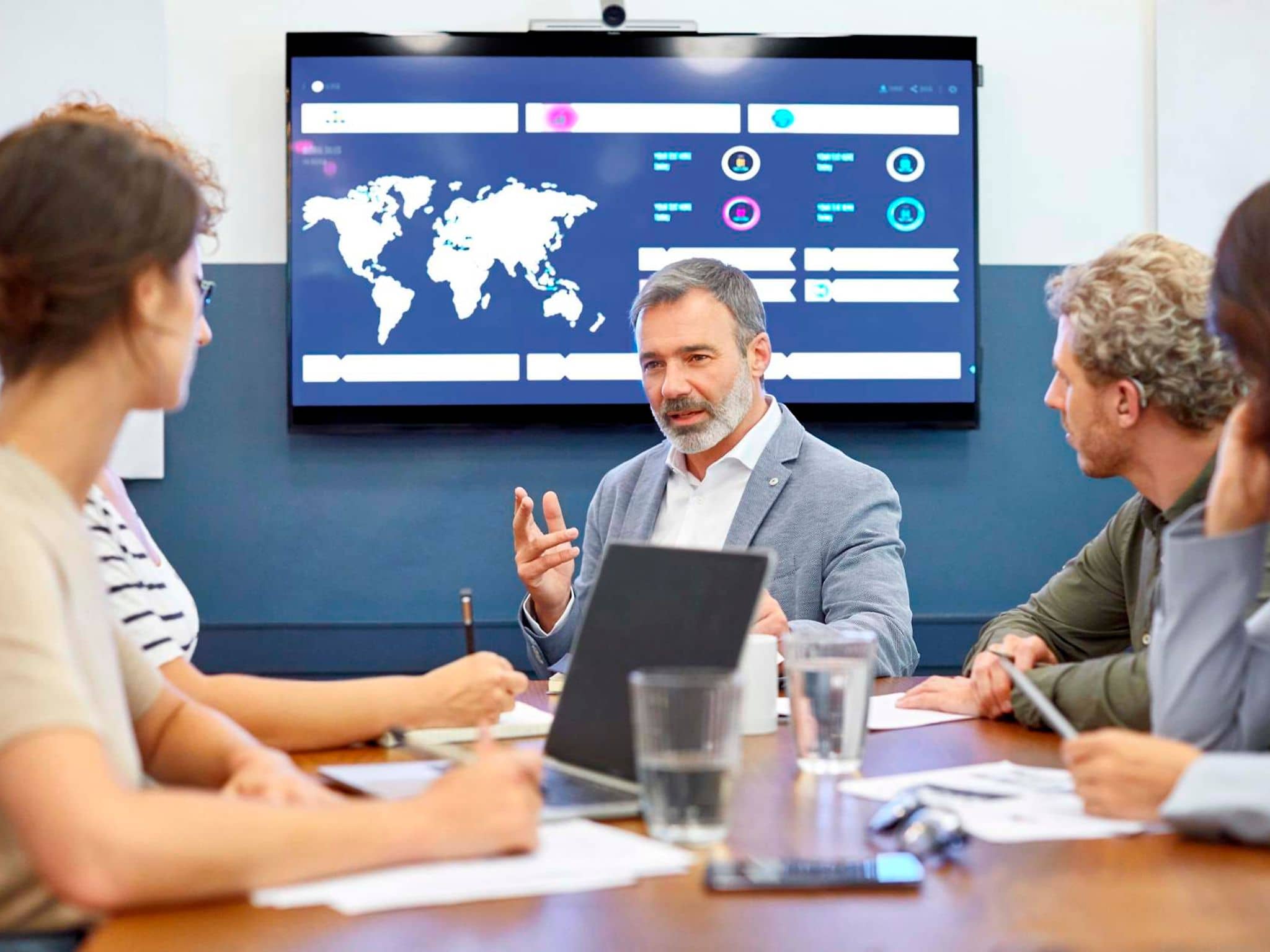 Bild: Personen am Konferenztisch mit einer Weltkarte im Hintergrund.