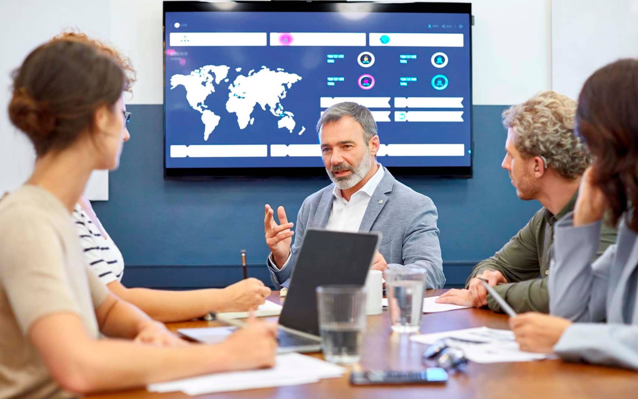Bild: Personen am Konferenztisch mit einer Weltkarte im Hintergrund.
