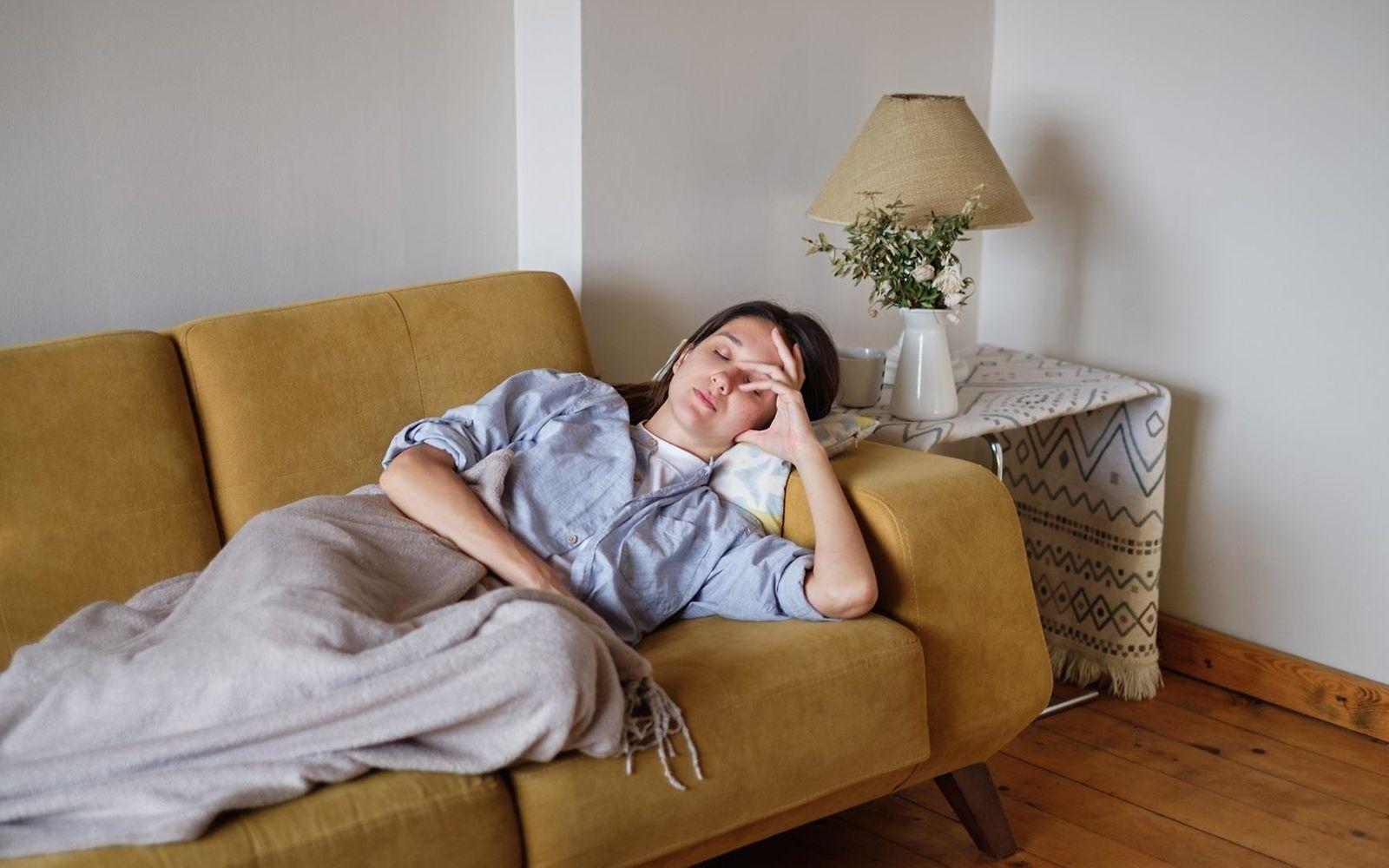 Symbolbild: Kranke Frau liegt auf dem Sofa und fasst sich an den Kopf