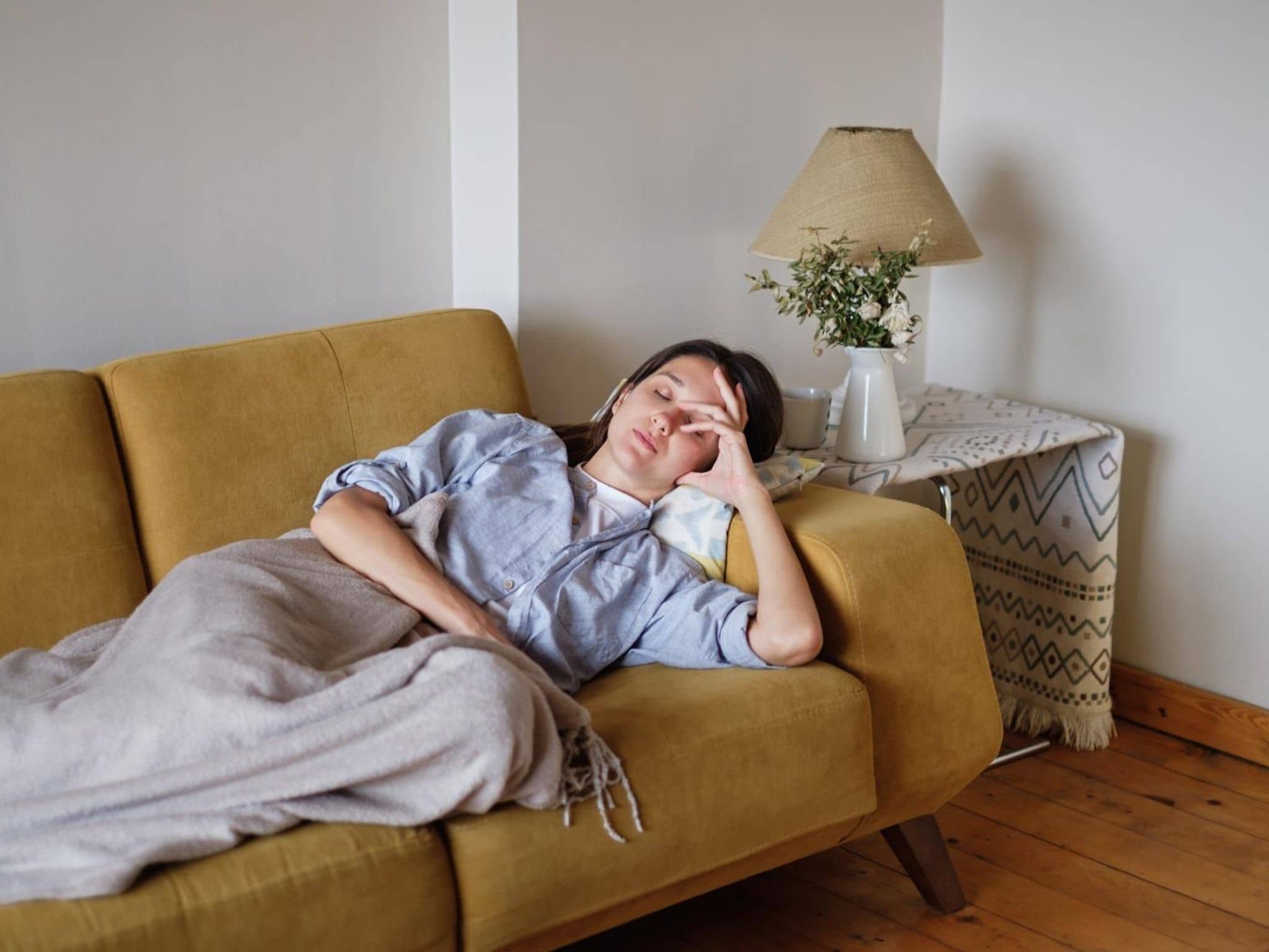 Symbolbild: Kranke Frau liegt auf dem Sofa und fasst sich an den Kopf