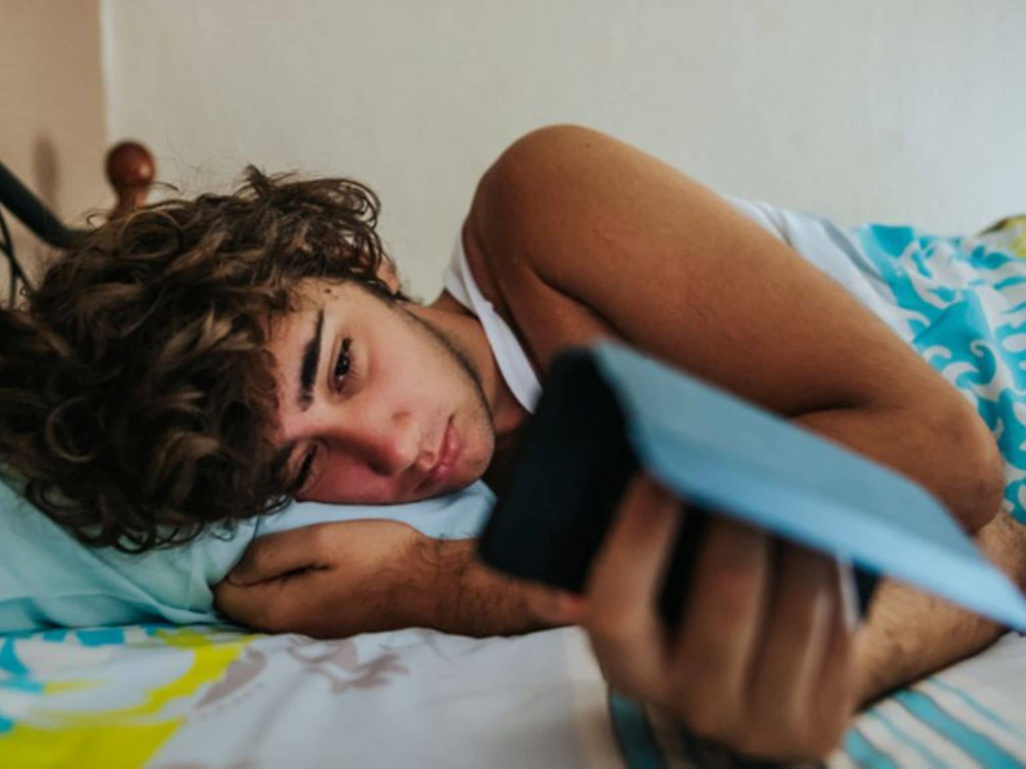 Ein Jugendlicher liegt im Bett und starrt in sein Handy, weil er nicht schlafen kann.