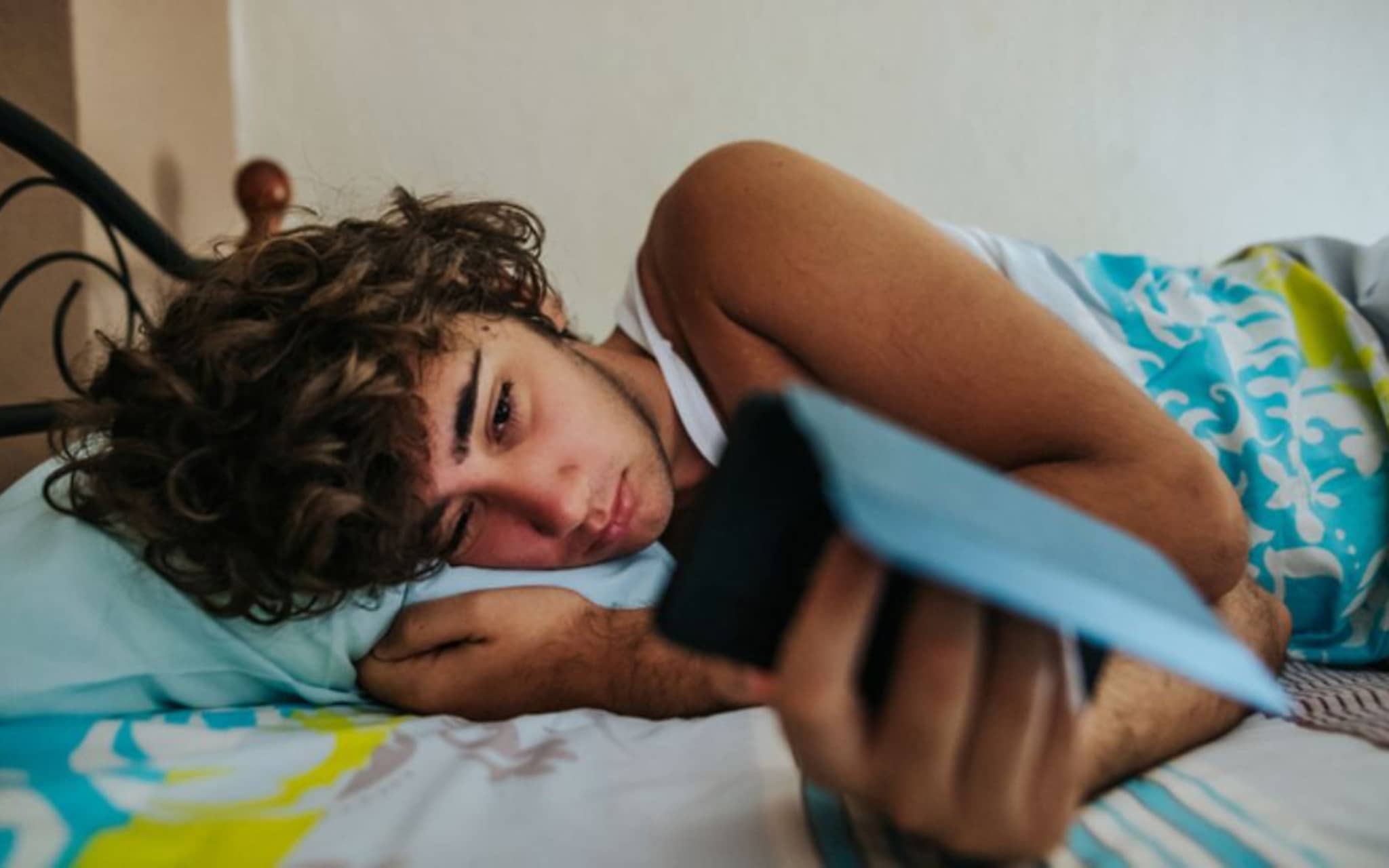 Ein Jugendlicher liegt im Bett und starrt in sein Handy, weil er nicht schlafen kann.