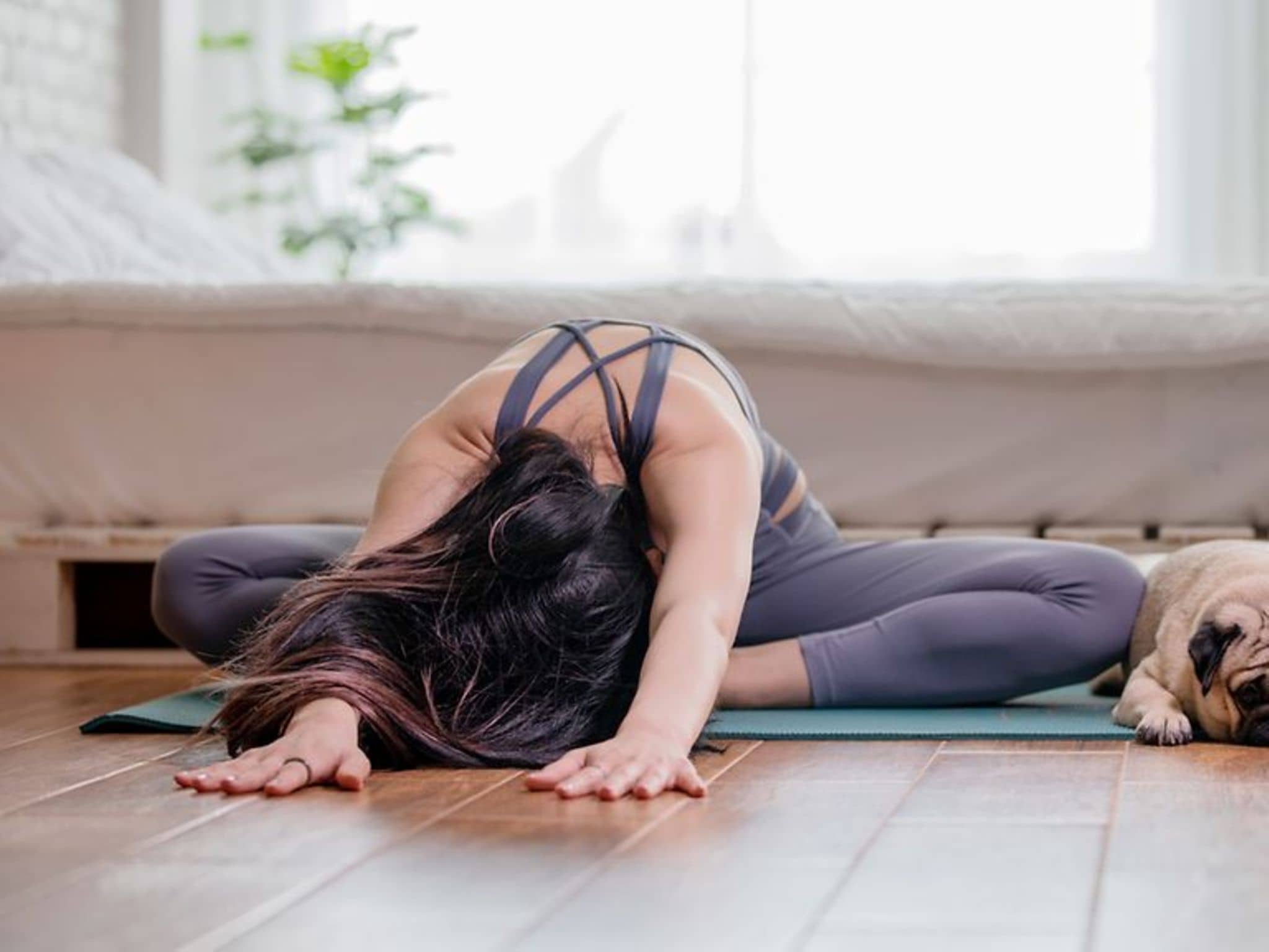 Frau sitzt im Schneidersitz auf einer Yogamatte, ihr Oberkörper liegt mit gestreckten Armen auf dem Boden