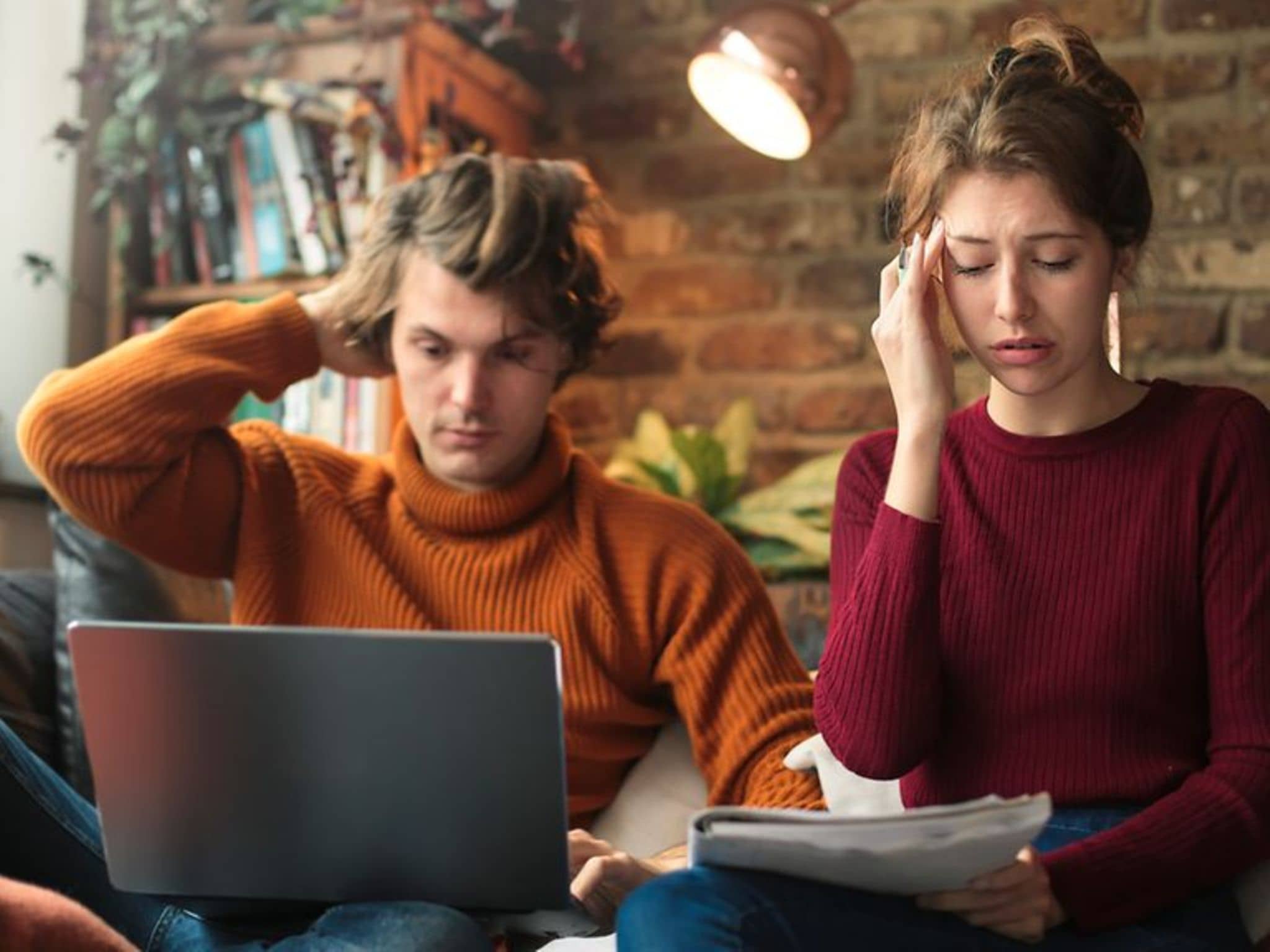 Mädchen und Junge sitzen auf der Couch mit ihren Laptops und wirken gestresst.