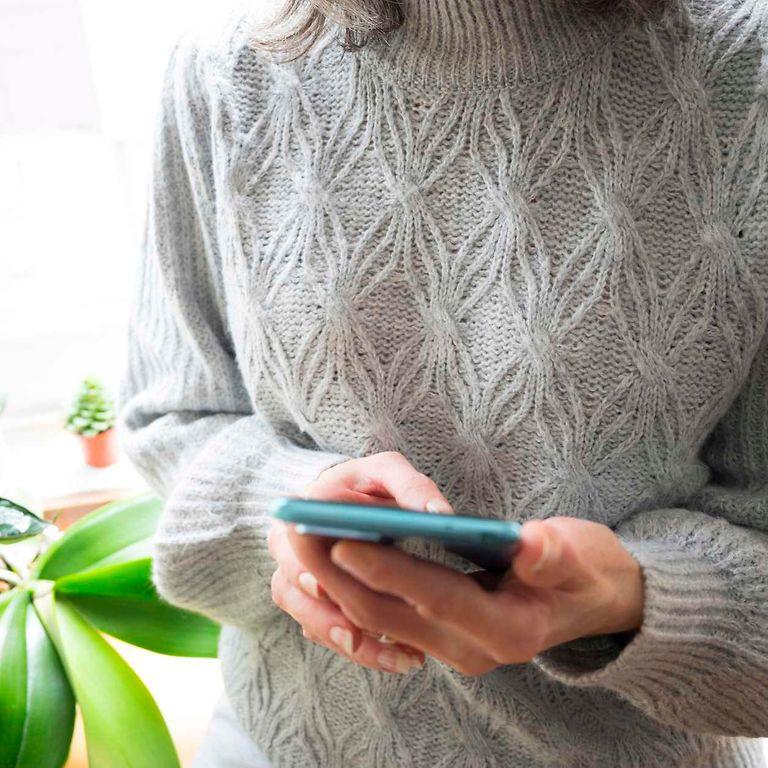 Bild: Frau mit Wollpullover hält ihr Handy in den Händen.