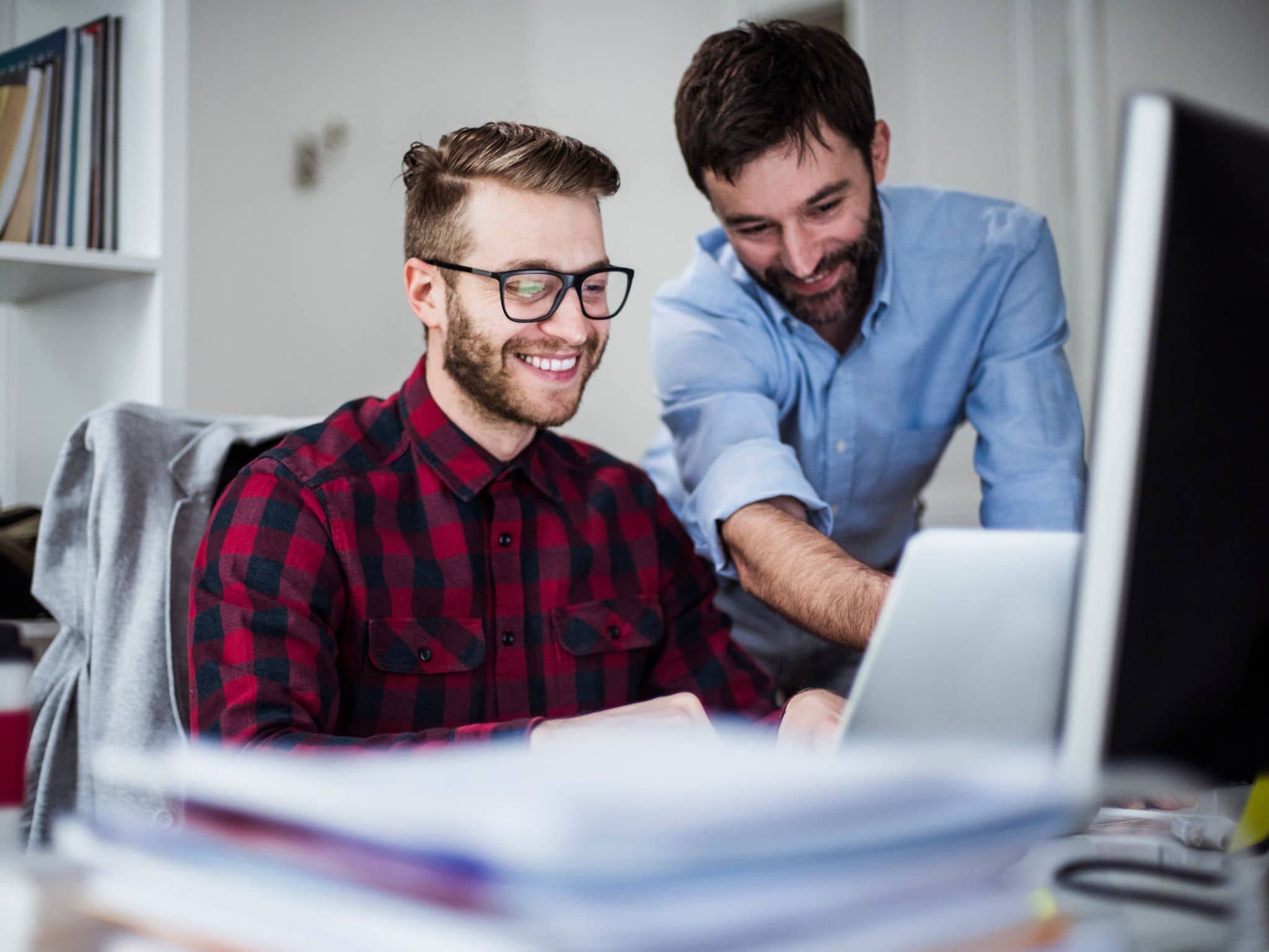 Bild: Mann zeigt einem Studierenden im Büro etwas am Laptop.