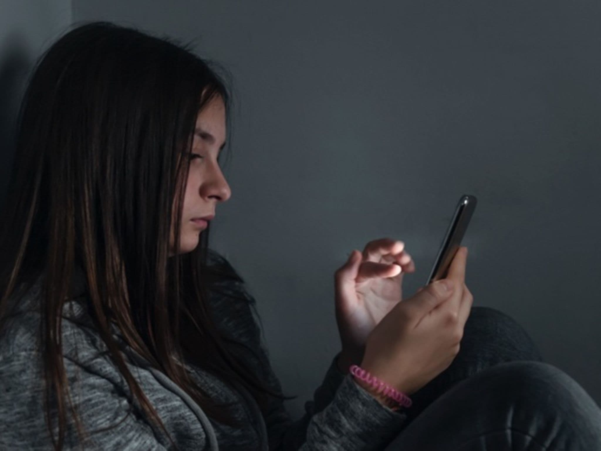 DAK Mediensuchtstudie 2023: Junges Mädchen sitzt in einem dunklen Raum und schaut auf Ihr Handy.