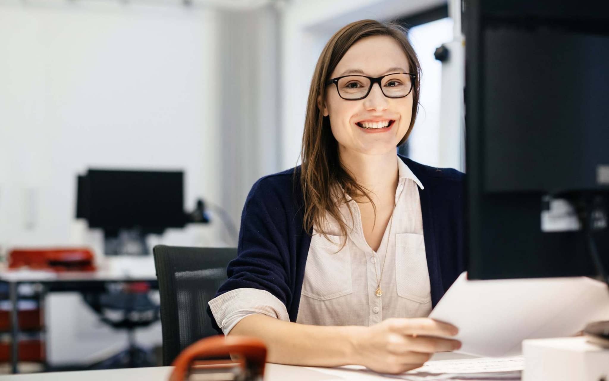Bild: Junge Frau mit Brille schaut etwas am Schreibtisch nach.