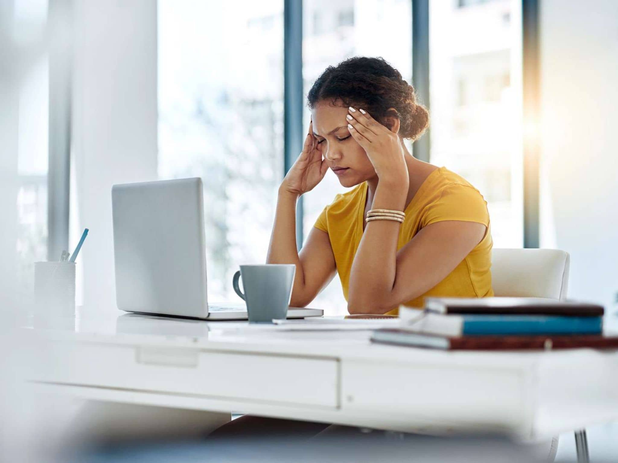 DAK-Psychreport: Erschöpft wirkende Frau sitzt vor einem Notebook und hält ihre Hände an die Schläfen.