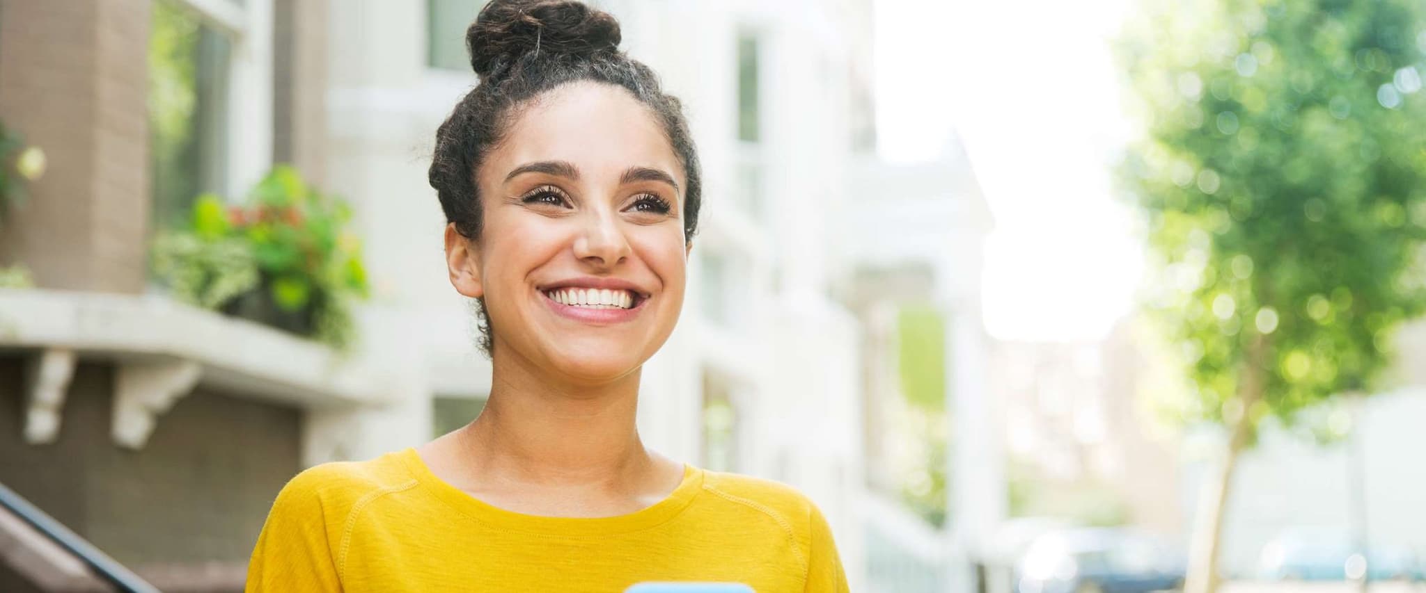 DAK Plus-Leistungen: Junge Frau steht auf der Straße und hält ihr Handy in der Hand.