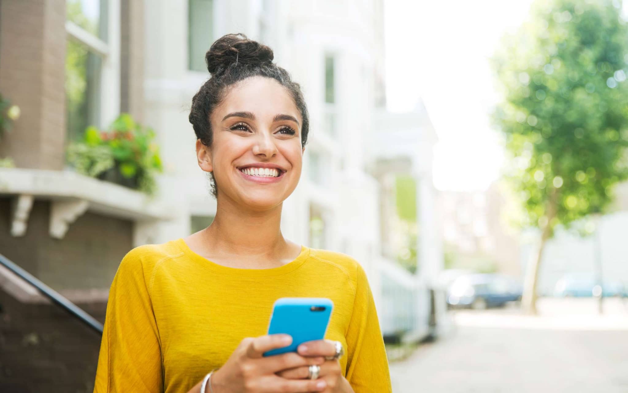 DAK Plus-Leistungen: Junge Frau steht auf der Straße und hält ihr Handy in der Hand.