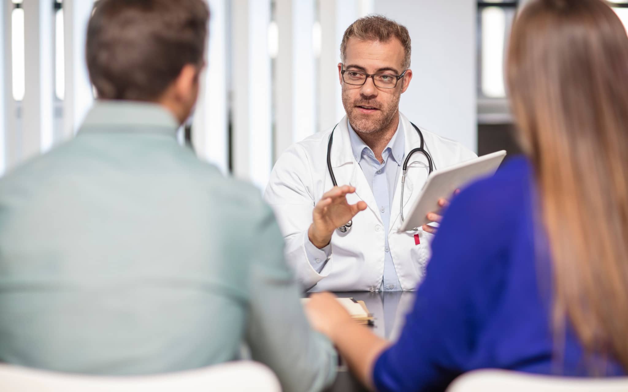 Verhütung für den Mann: Ein Paar sitzt in einer Arztpraxis und führt ein Gespräch mit einem Arzt