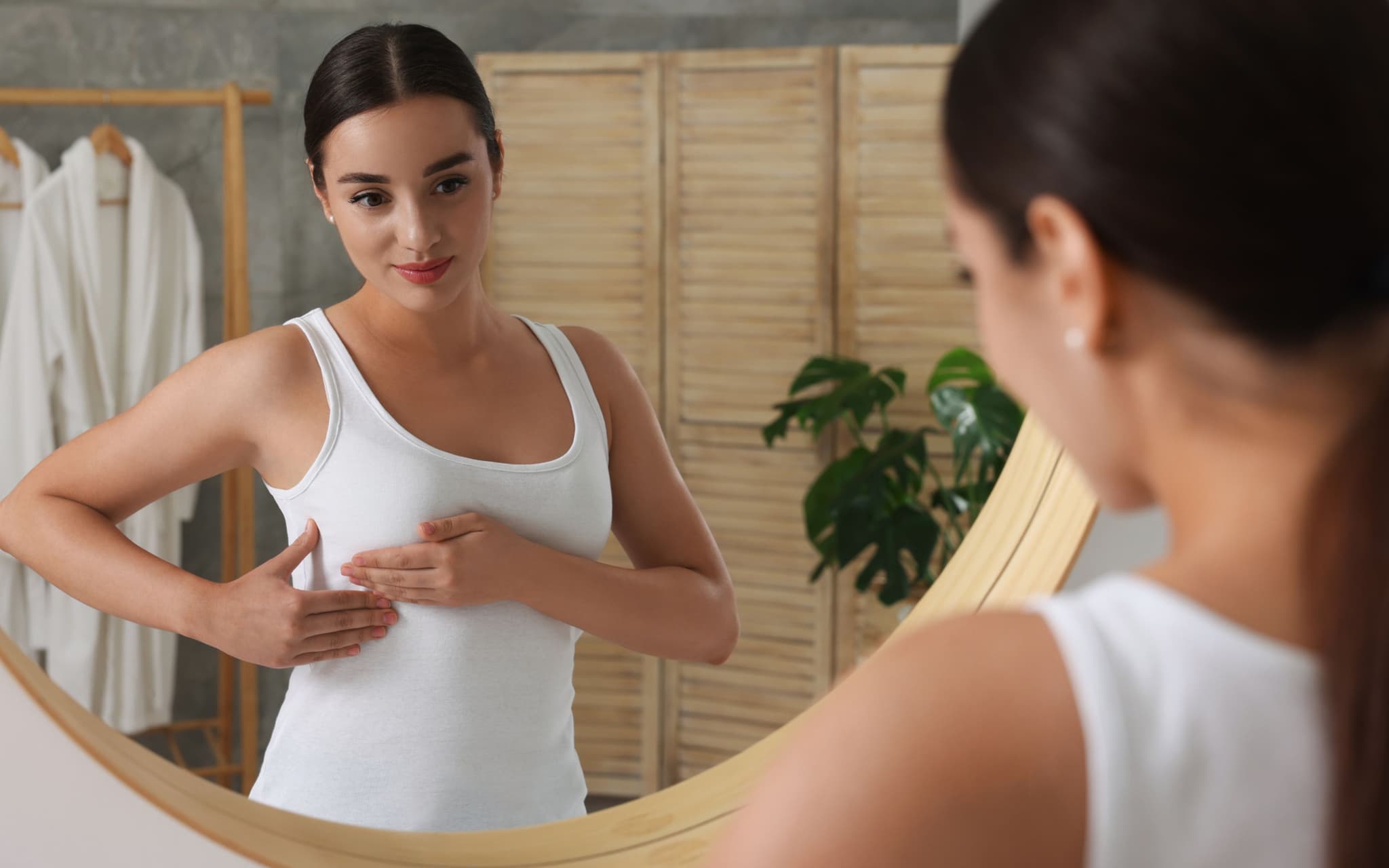 Brust abtasten: Eine Frau steht vor dem Spiegel und tastet ihre Brust ab