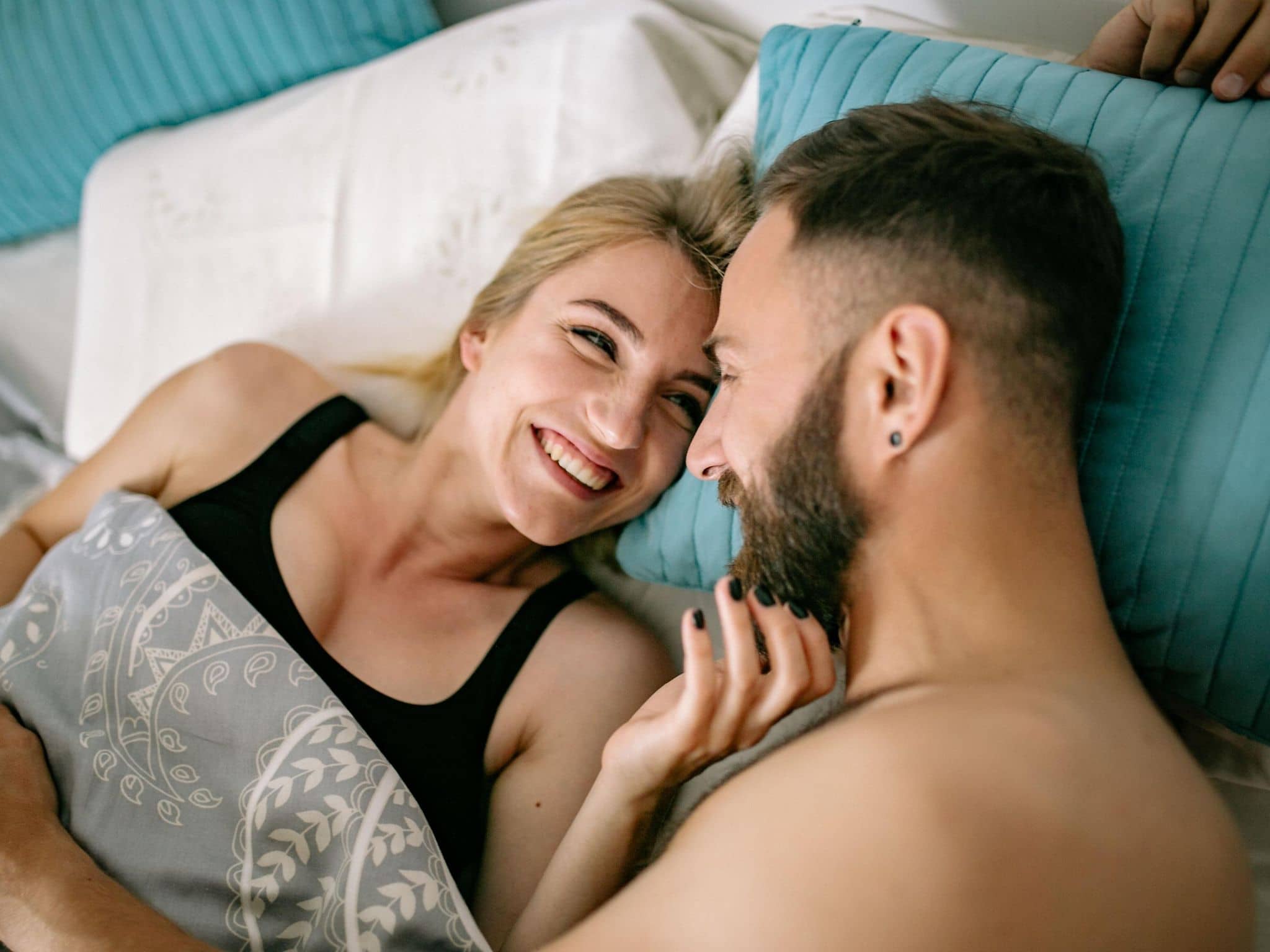 Junges Paar liegt im Bett und liebkost sich.