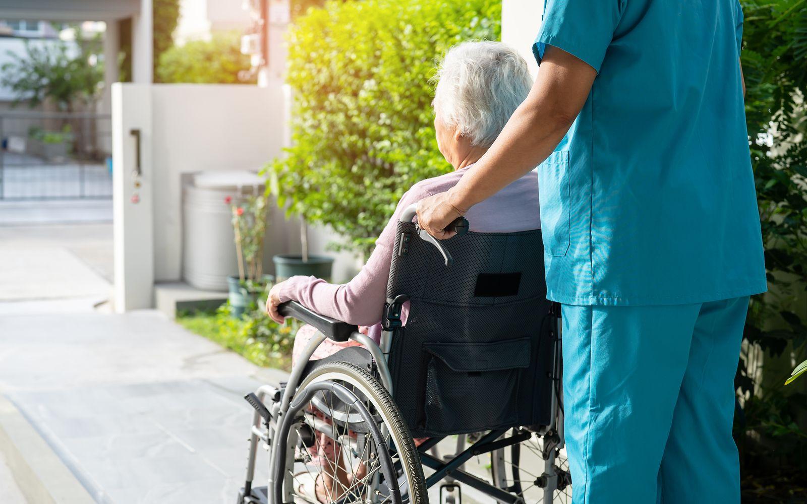 Hilfsmittel: Eine Seniorin sitzt im Rollstuhl und wird geschoben