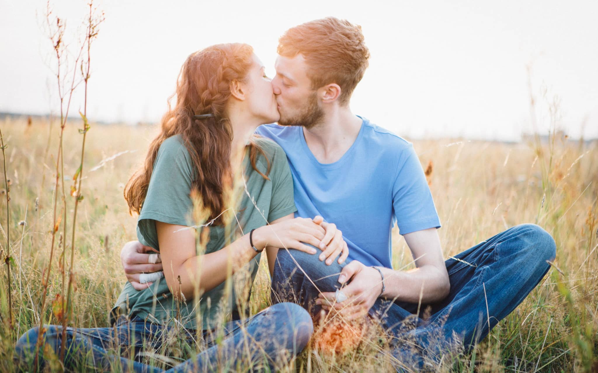 Ab wann bin ich bereit für Sex? Ein junges Mädchen und ein Jugendlicher sitzen auf einer Wiese uns küssen sich