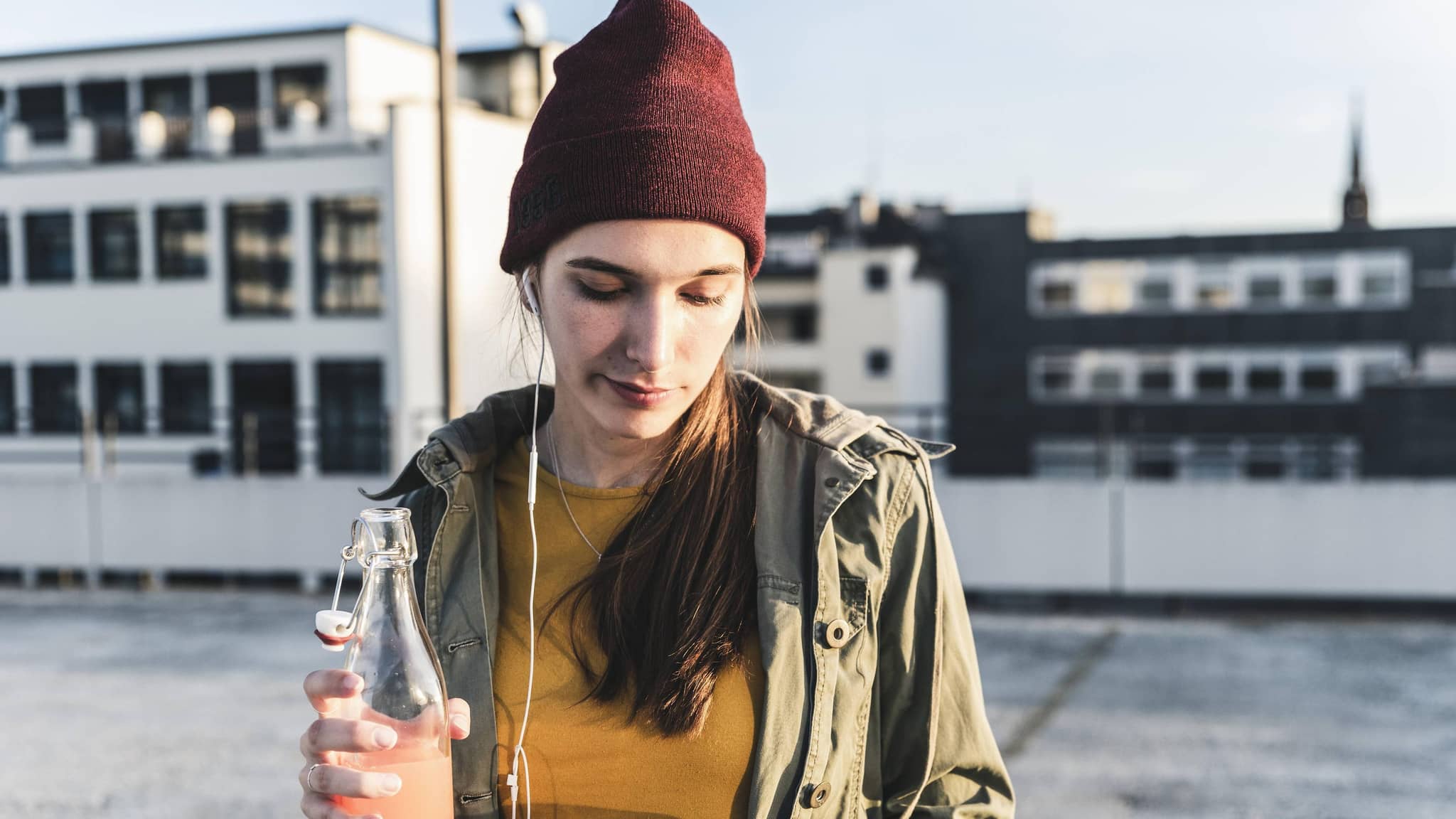 Junge Frau mit Drink und Handy in der Hand auf einem Parkdeck.